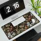 A rectangular desk mat with a William Morris & Co floral pattern in multiple colours, placed under a desk with a keyboard and mouse on top.