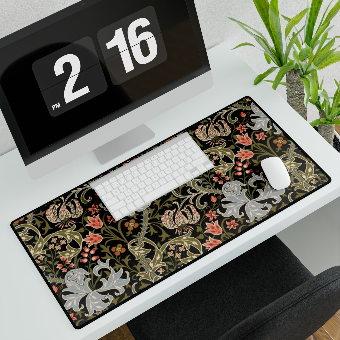 A rectangular desk mat with a William Morris & Co floral pattern in multiple colours, placed under a desk with a keyboard and mouse on top.