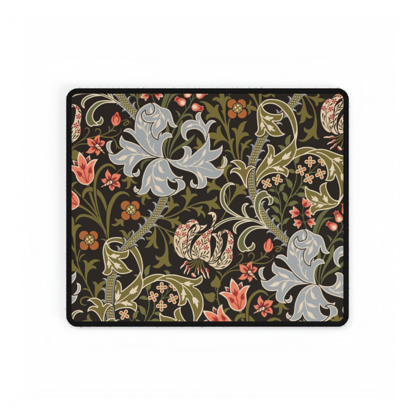 A rectangular desk mat with a William Morris & Co floral pattern in multiple colours, placed under a desk with a keyboard and mouse on top.