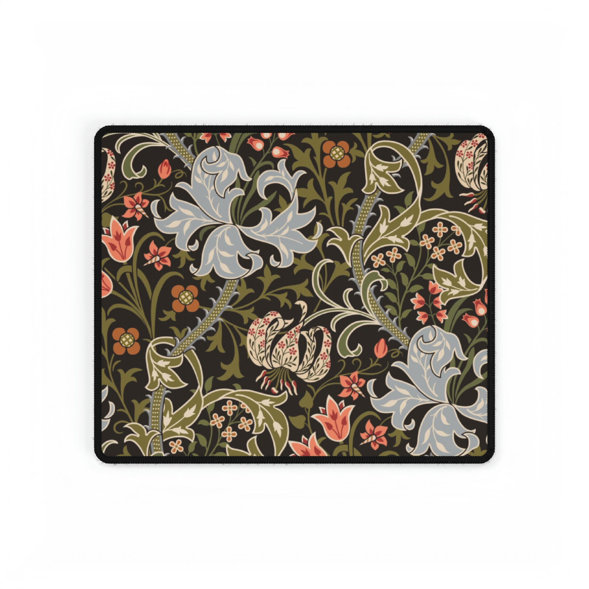 A rectangular desk mat with a William Morris & Co floral pattern in multiple colours, placed under a desk with a keyboard and mouse on top.