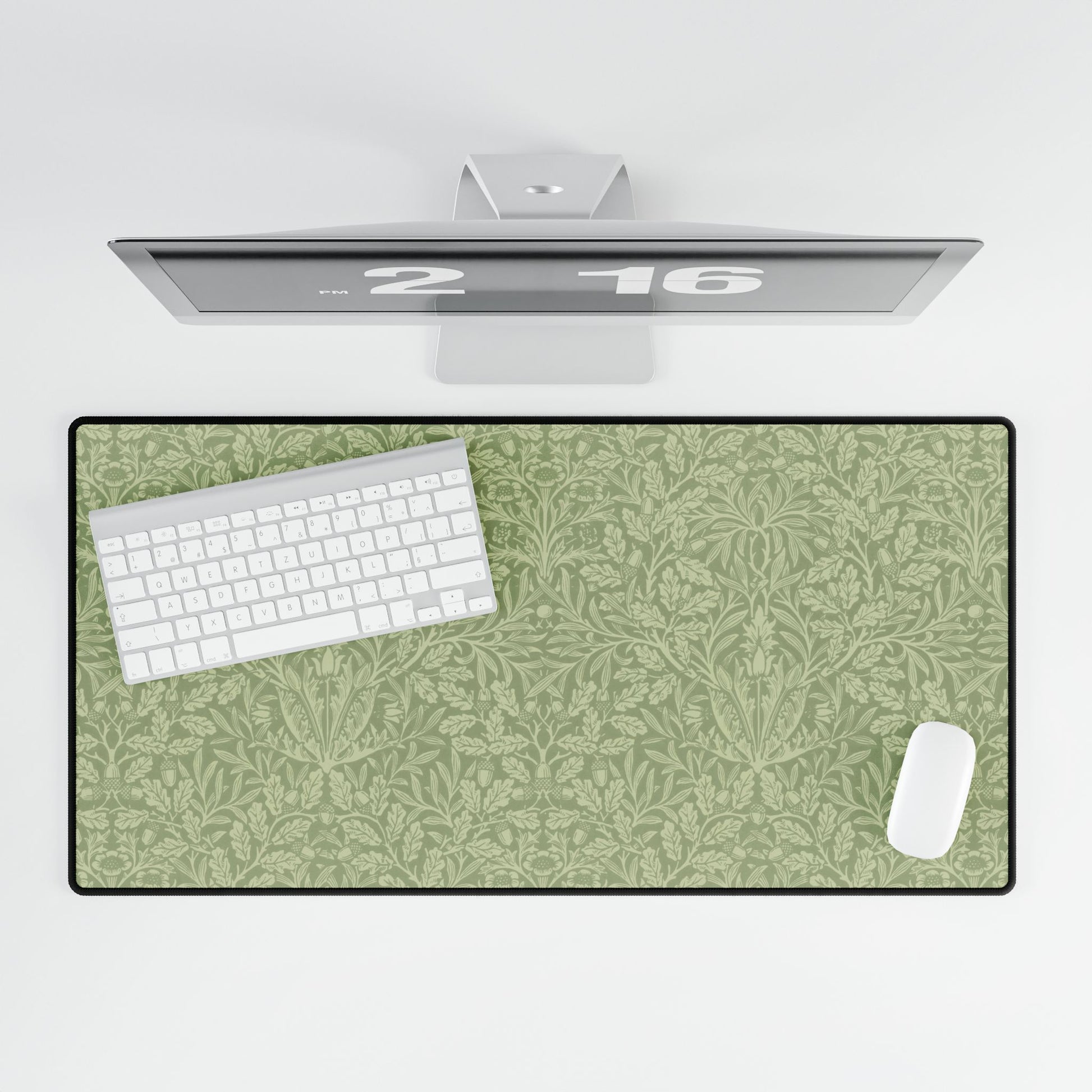 A rectangular desk mat with a green floral pattern, featuring a William Morris & Co oak leaf design, placed under a white desk lamp and a computer mouse on top of the mat.