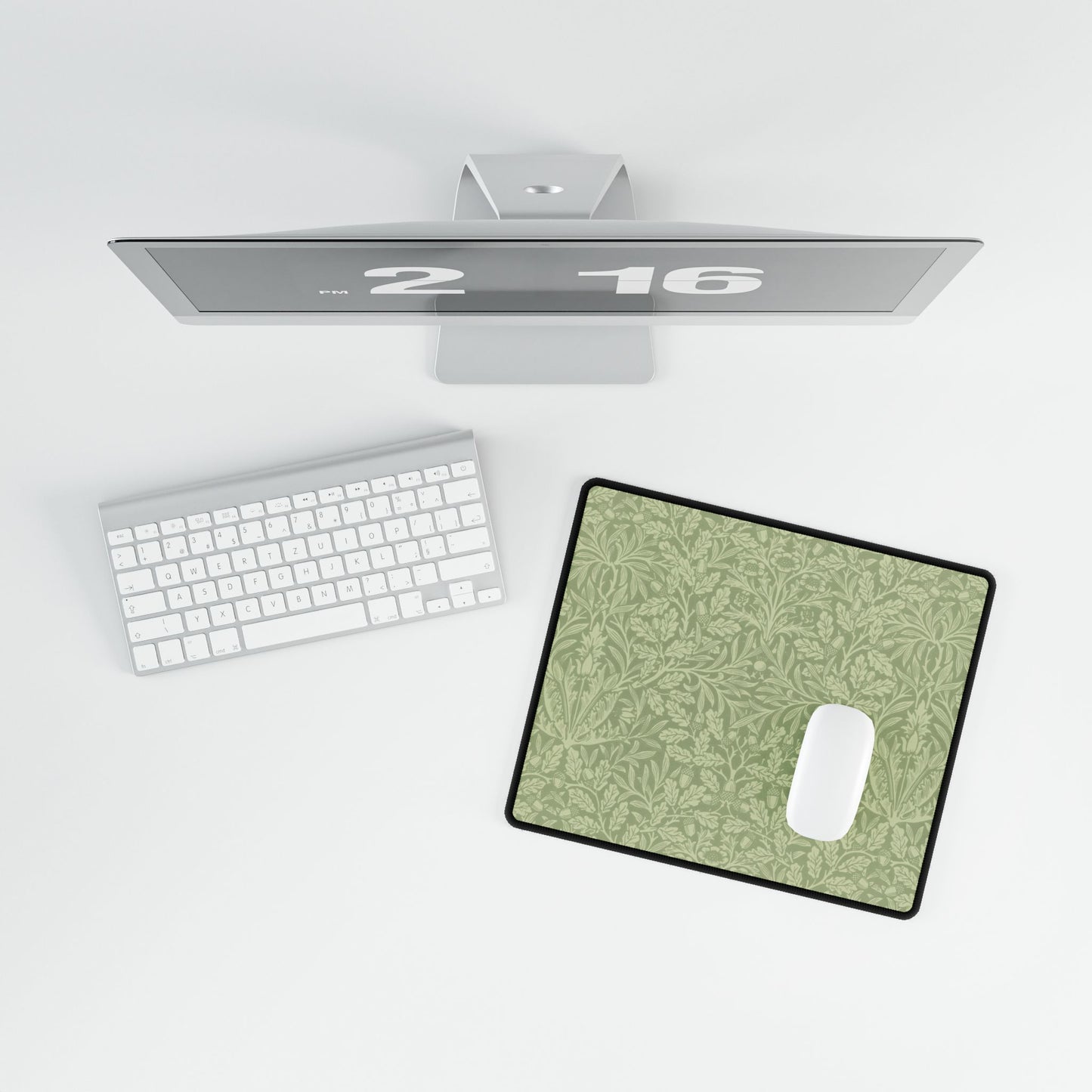 A rectangular desk mat with a green floral pattern, featuring a William Morris & Co oak leaf design, placed under a white desk lamp and a computer mouse on top of the mat.