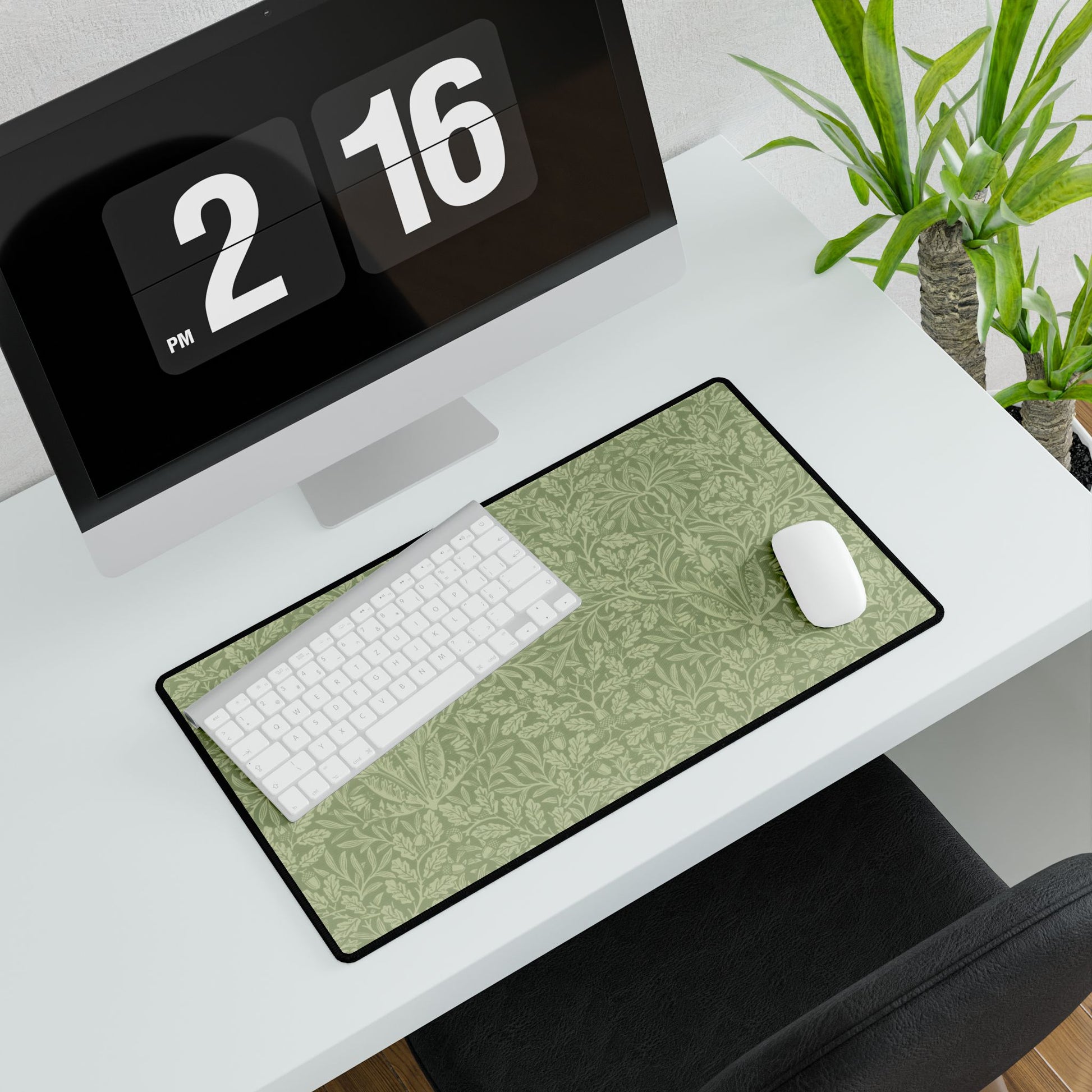A rectangular desk mat with a green floral pattern, featuring a William Morris & Co oak leaf design, placed under a white desk lamp and a computer mouse on top of the mat.