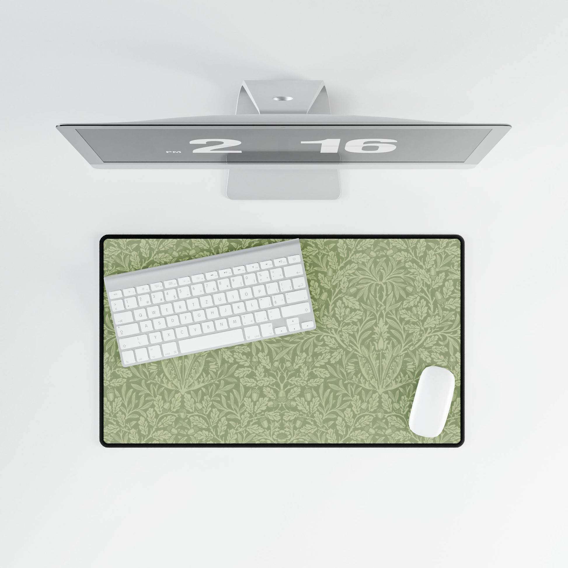 A rectangular desk mat with a green floral pattern, featuring a William Morris & Co oak leaf design, placed under a white desk lamp and a computer mouse on top of the mat.