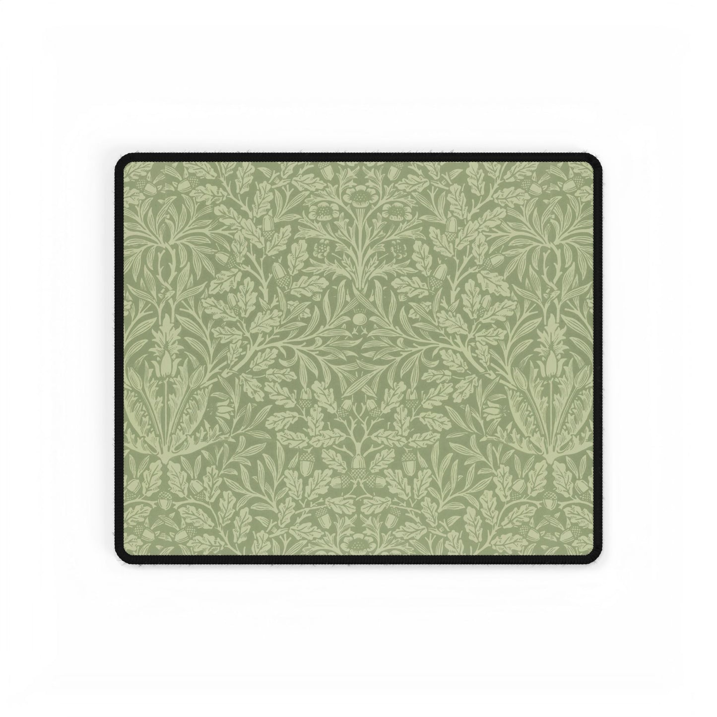 A rectangular desk mat with a green floral pattern, featuring a William Morris & Co oak leaf design, placed under a white desk lamp and a computer mouse on top of the mat.