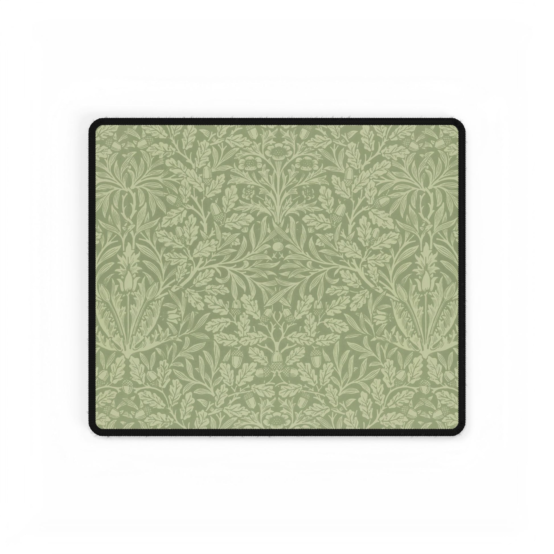 A rectangular desk mat with a green floral pattern, featuring a William Morris & Co oak leaf design, placed under a white desk lamp and a computer mouse on top of the mat.