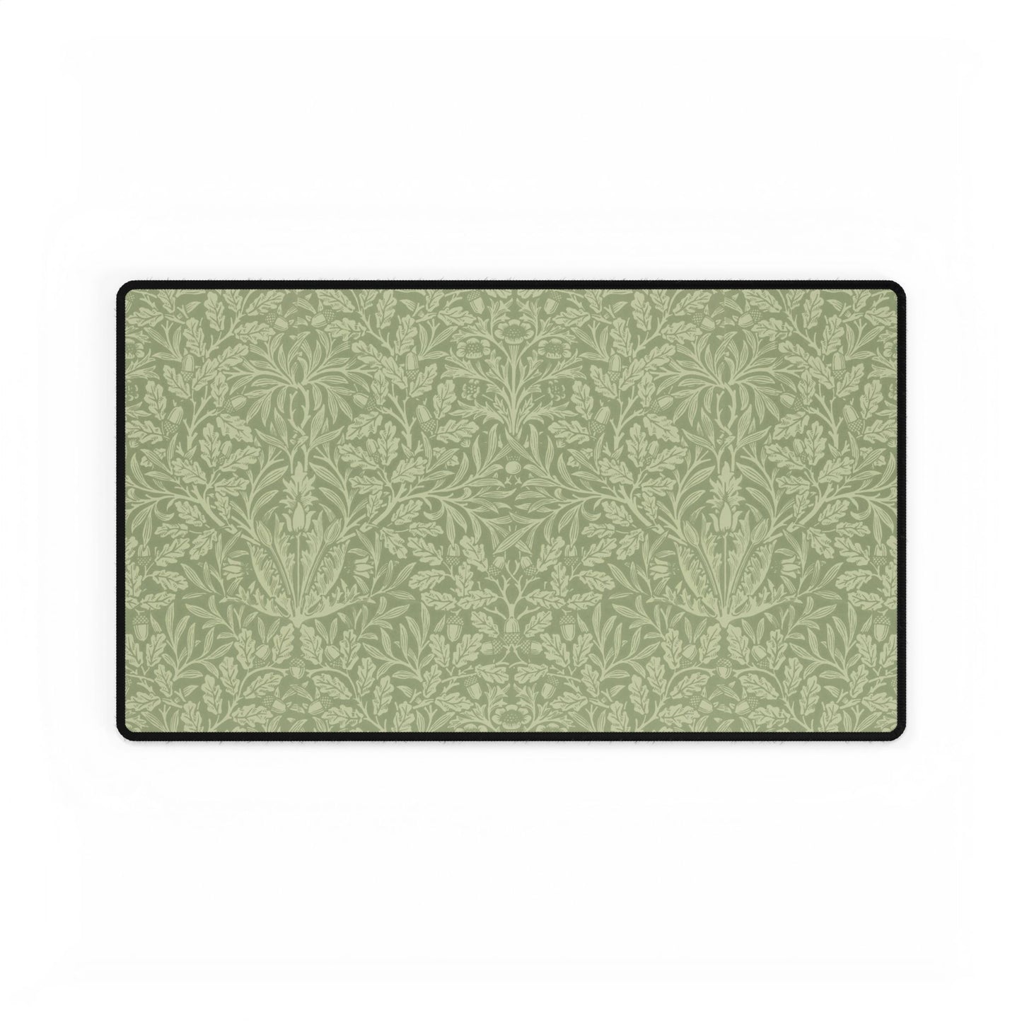 A rectangular desk mat with a green floral pattern, featuring a William Morris & Co oak leaf design, placed under a white desk lamp and a computer mouse on top of the mat.