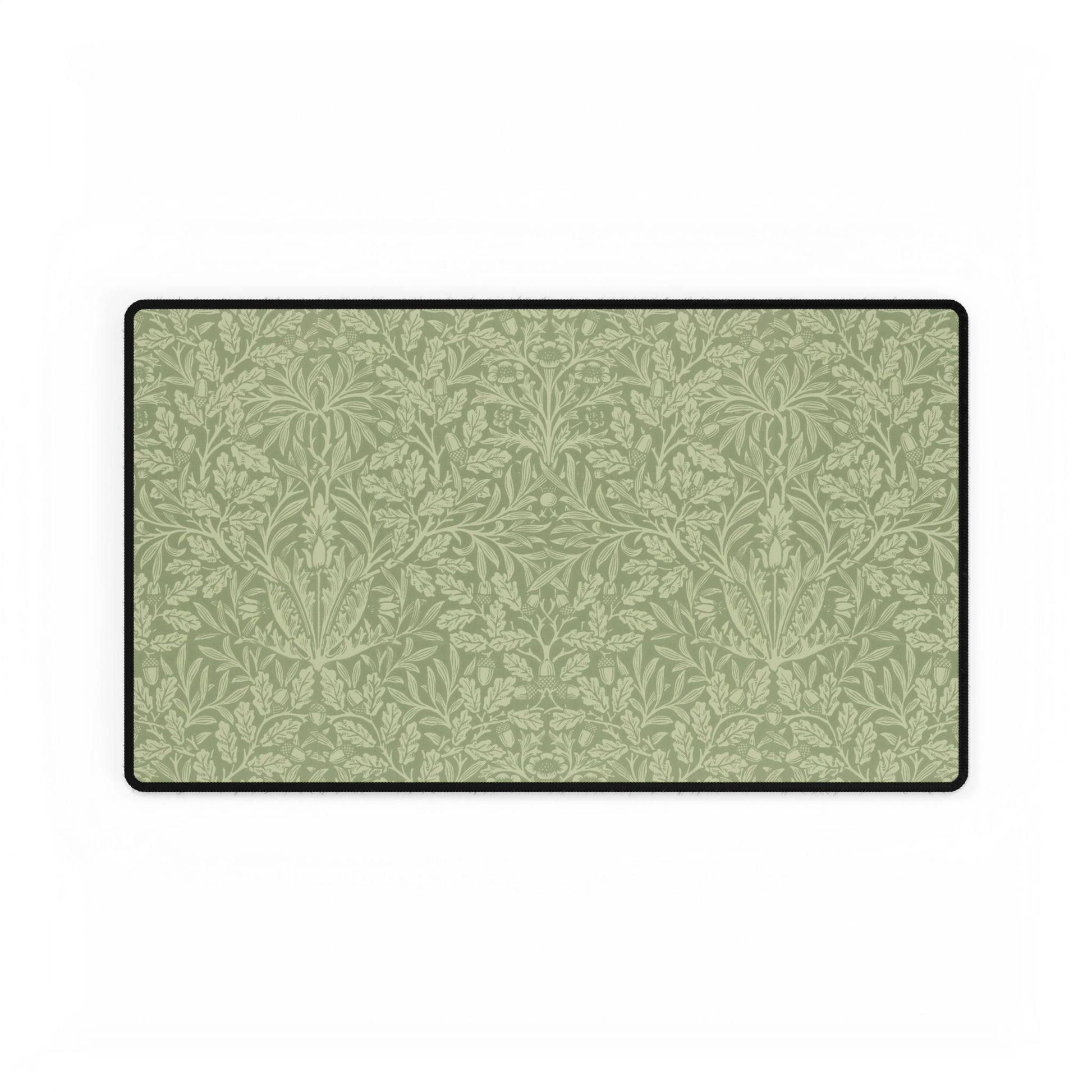 A rectangular desk mat with a green floral pattern, featuring a William Morris & Co oak leaf design, placed under a white desk lamp and a computer mouse on top of the mat.