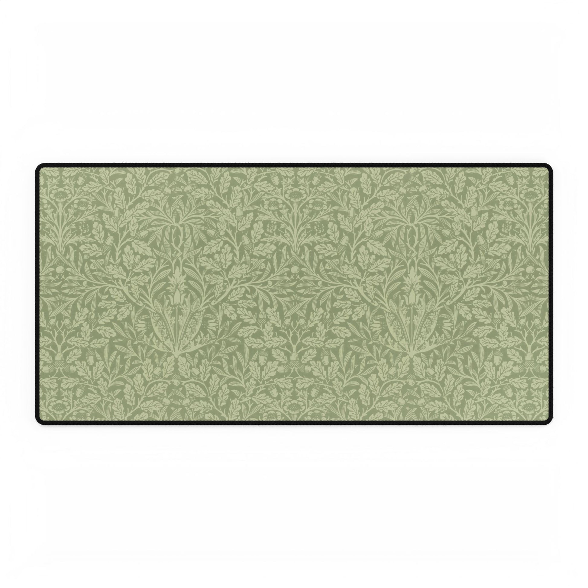 A rectangular desk mat with a green floral pattern, featuring a William Morris & Co oak leaf design, placed under a white desk lamp and a computer mouse on top of the mat.