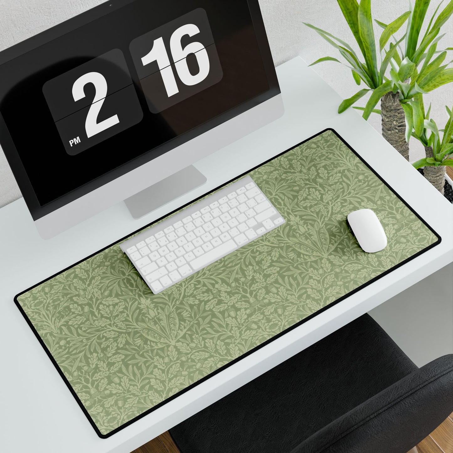 A rectangular desk mat with a green floral pattern, featuring a William Morris & Co oak leaf design, placed under a white desk lamp and a computer mouse on top of the mat.