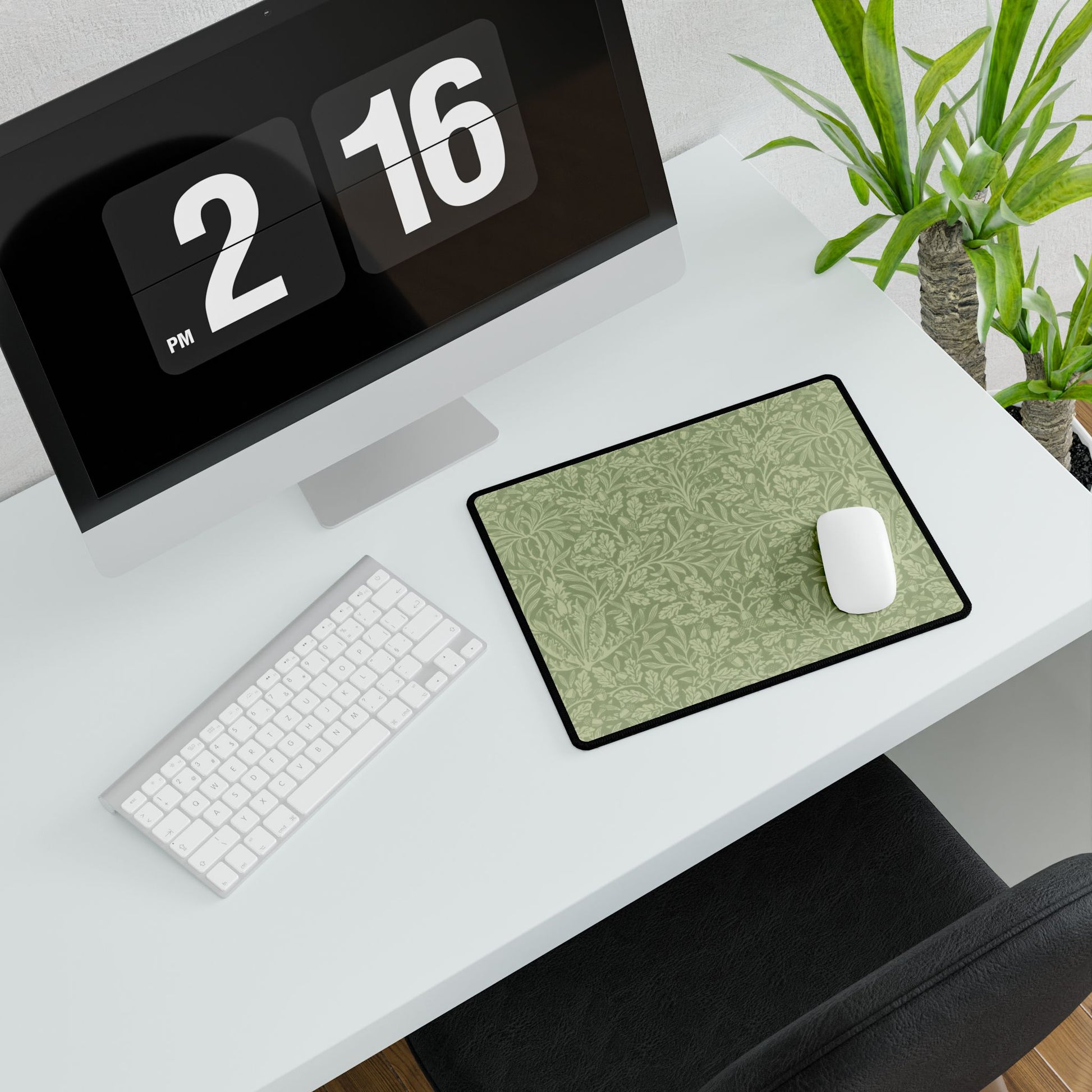 A rectangular desk mat with a green floral pattern, featuring a William Morris & Co oak leaf design, placed under a white desk lamp and a computer mouse on top of the mat.