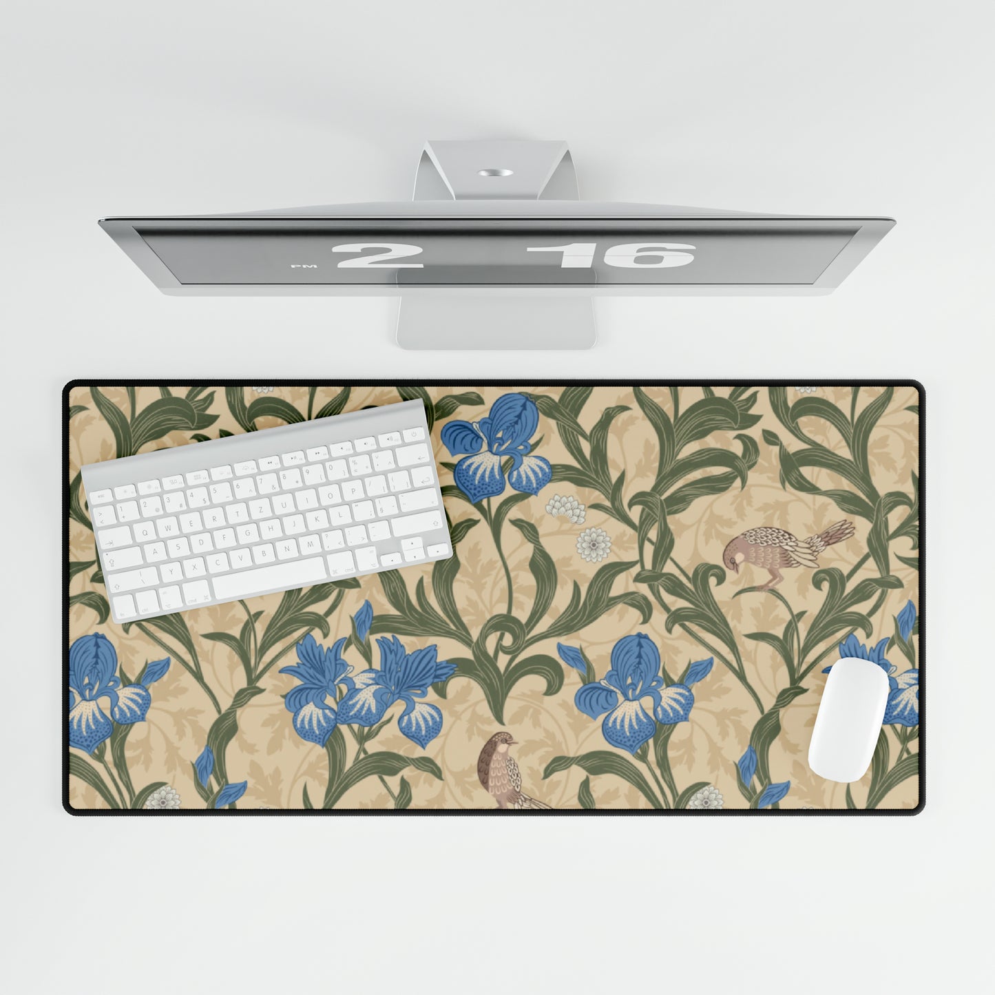 A desk mat with a floral pattern, primarily in blue and green shades, placed under a white desk surface with a keyboard and a computer mouse on top.