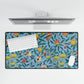 A desk mat with a floral pattern featuring various fruits, placed under a desk with a keyboard and mouse on top.