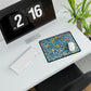 A desk mat with a floral pattern featuring various fruits, placed under a desk with a keyboard and mouse on top.