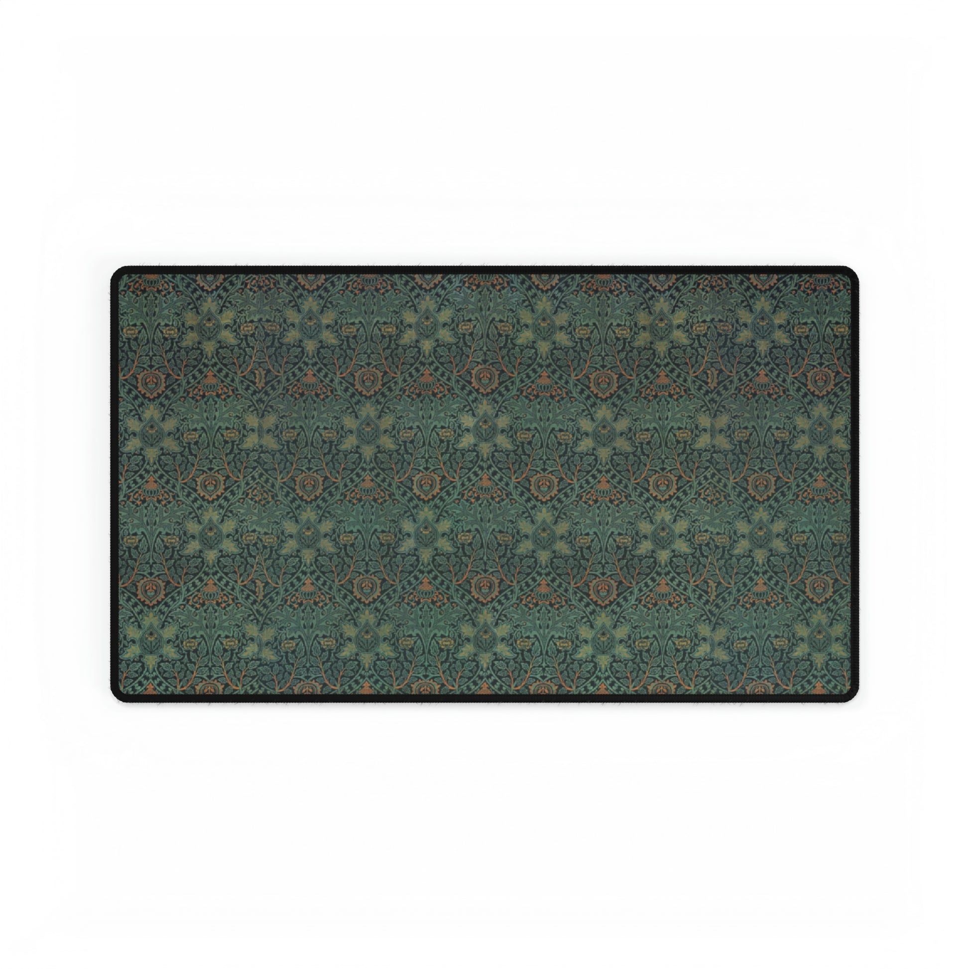 A rectangular desk mat with a William Morris & Co floral pattern in green, brown, and white, placed under a white desk and a keyboard.