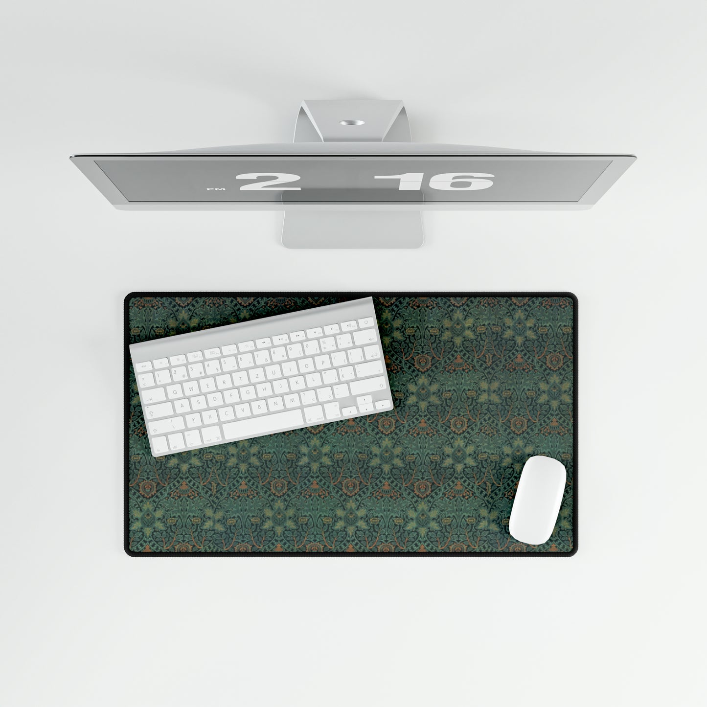A rectangular desk mat with a William Morris & Co floral pattern in green, brown, and white, placed under a white desk and a keyboard.