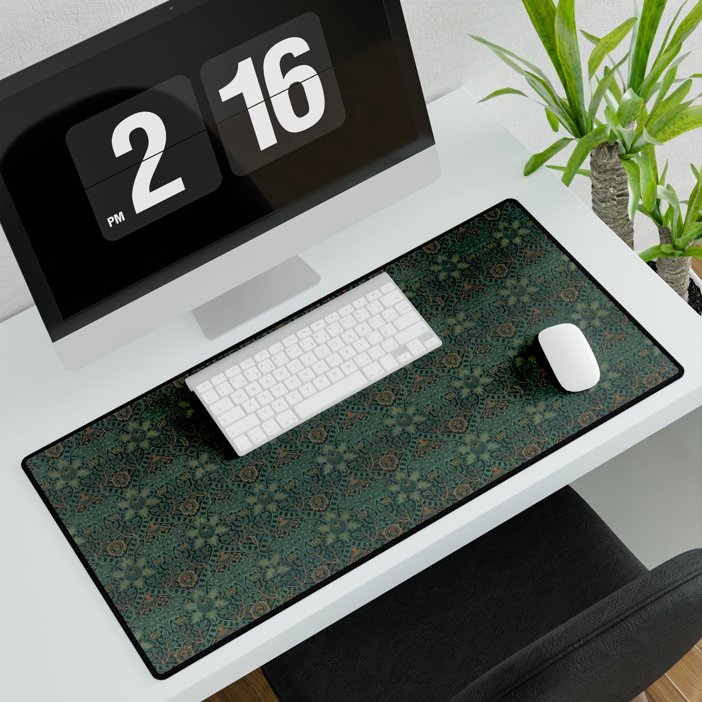 A rectangular desk mat with a William Morris & Co floral pattern in green, brown, and white, placed under a white desk and a keyboard.