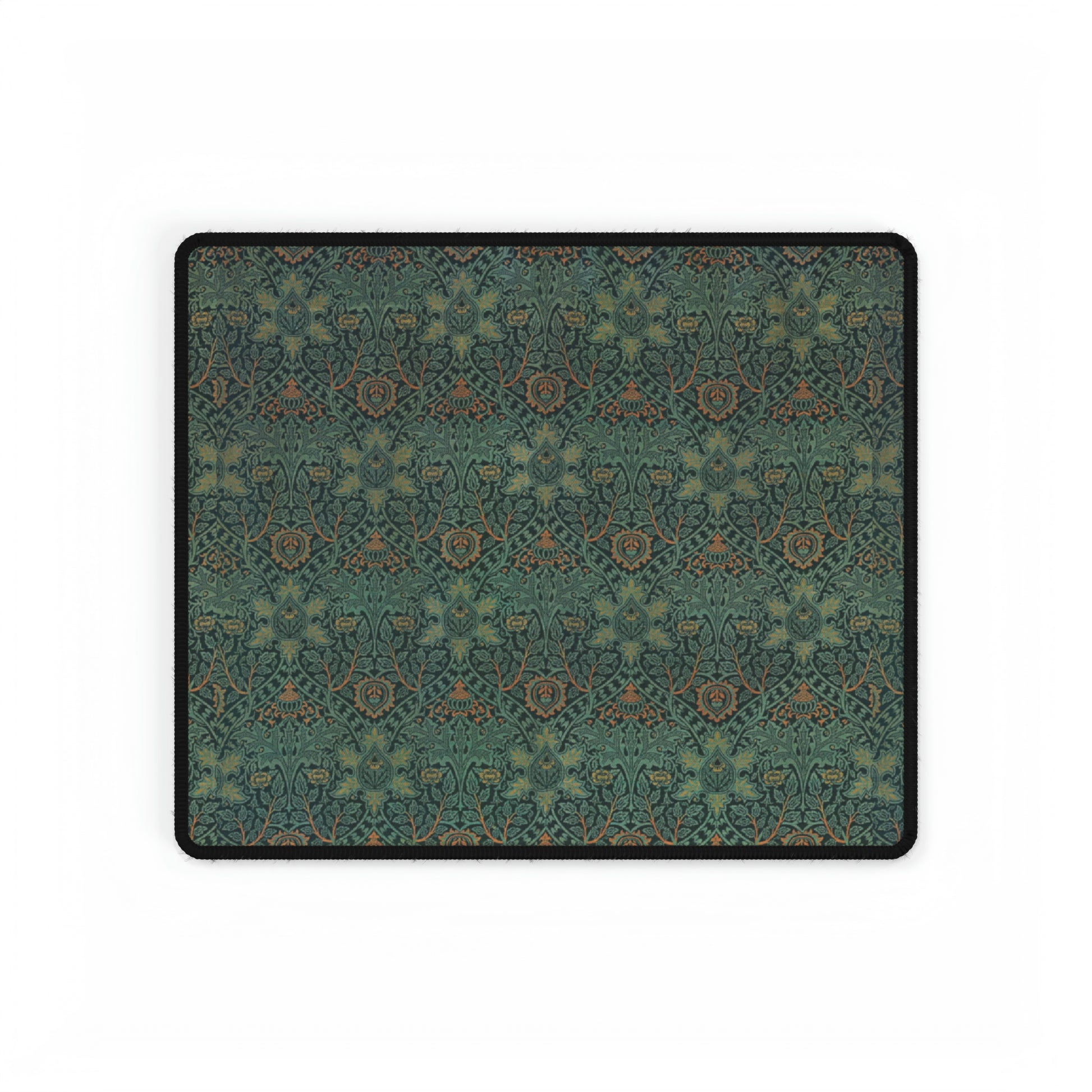 A rectangular desk mat with a William Morris & Co floral pattern in green, brown, and white, placed under a white desk and a keyboard.