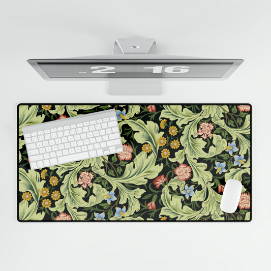 A large desk mat with a green William Morris & Co floral pattern, displayed on a desk with a keyboard and mouse, with a monitor above it.