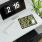 A large desk mat with a green William Morris & Co floral pattern, displayed on a desk with a keyboard and mouse, with a monitor above it.