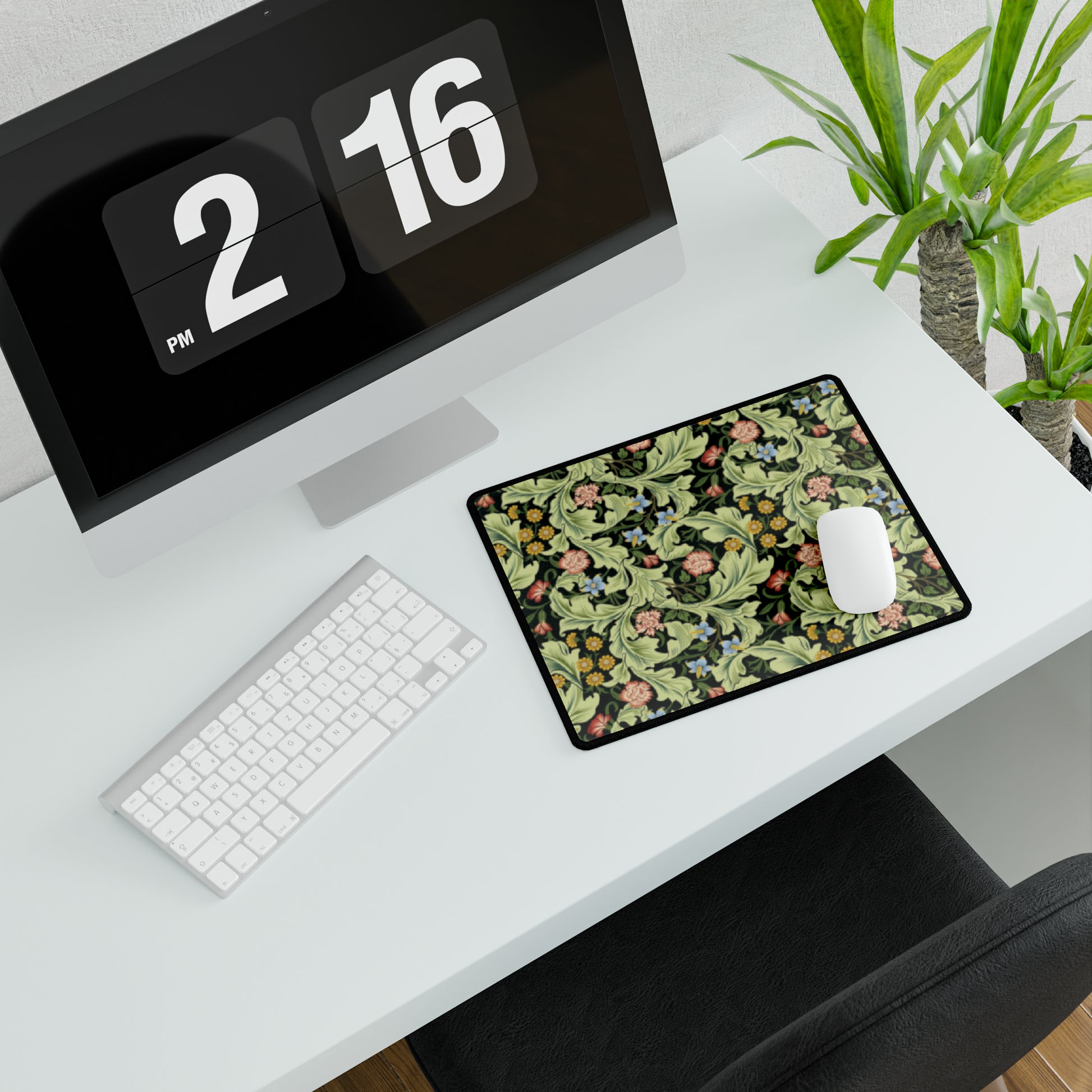 A large desk mat with a green William Morris & Co floral pattern, displayed on a desk with a keyboard and mouse, with a monitor above it.