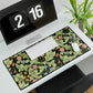 A large desk mat with a green William Morris & Co floral pattern, displayed on a desk with a keyboard and mouse, with a monitor above it.