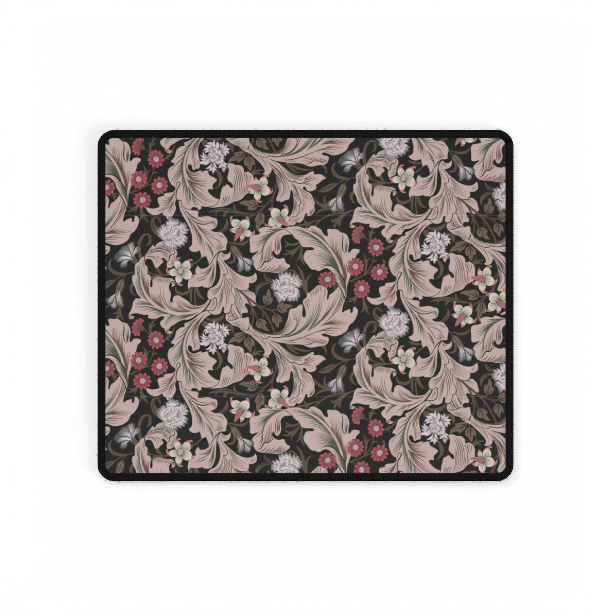 A large desk mat with a William Morris & Co floral pattern in mocha and black colours, displayed on a desk with a keyboard and mouse.