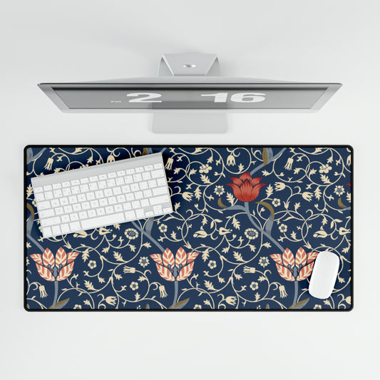 A large desk mat with a floral pattern in shades of red, pink and blue on a dark background, displayed under a monitor with a keyboard and mouse on top.