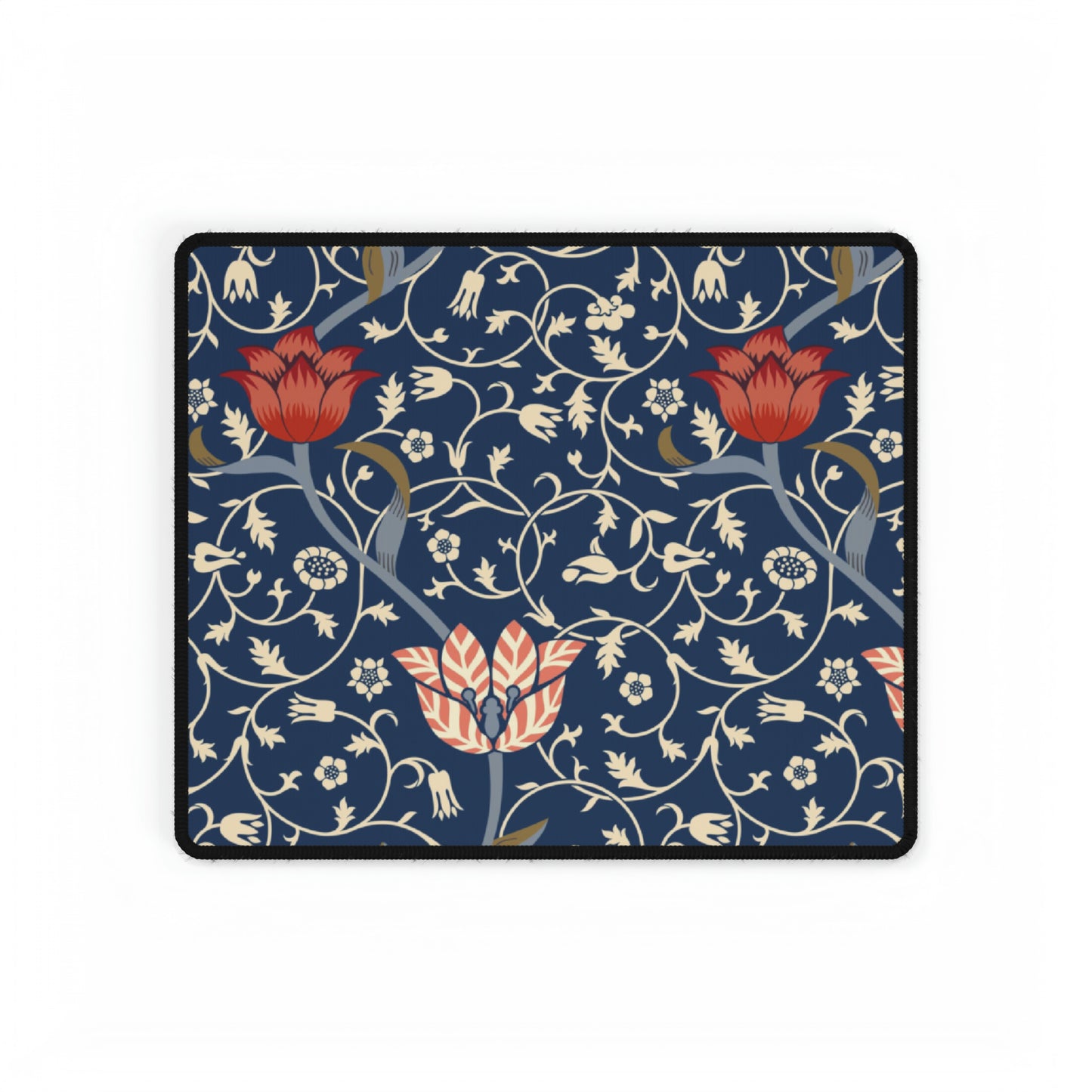 A large desk mat with a floral pattern in shades of red, pink and blue on a dark background, displayed under a monitor with a keyboard and mouse on top.