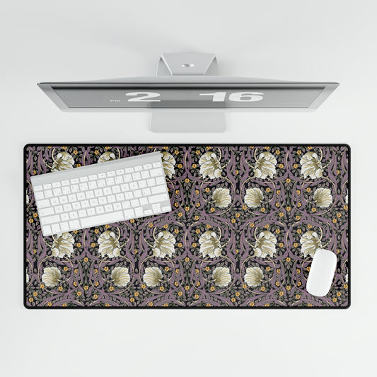 A large desk mat with a William Morris & Co floral pattern, displayed on a desk with a keyboard and mouse, with a monitor above it showing a part of the mat.