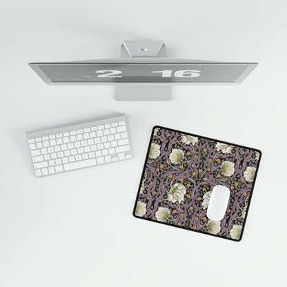 A large desk mat with a floral pattern, displayed on a desk with a keyboard and mouse, with a monitor above it showing a part of the mat.