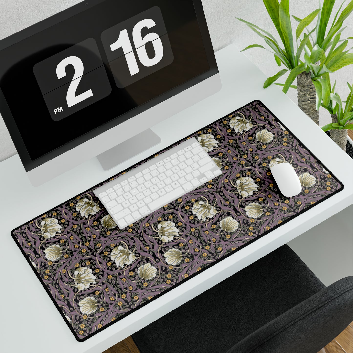 A large desk mat with a William Morris & Co floral pattern, displayed on a desk with a keyboard and mouse, with a monitor above it showing a part of the mat.