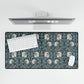 A large desk mat with a William Morris & Co floral pattern in shades of gray and blue, displayed on a desk with a keyboard and mouse.