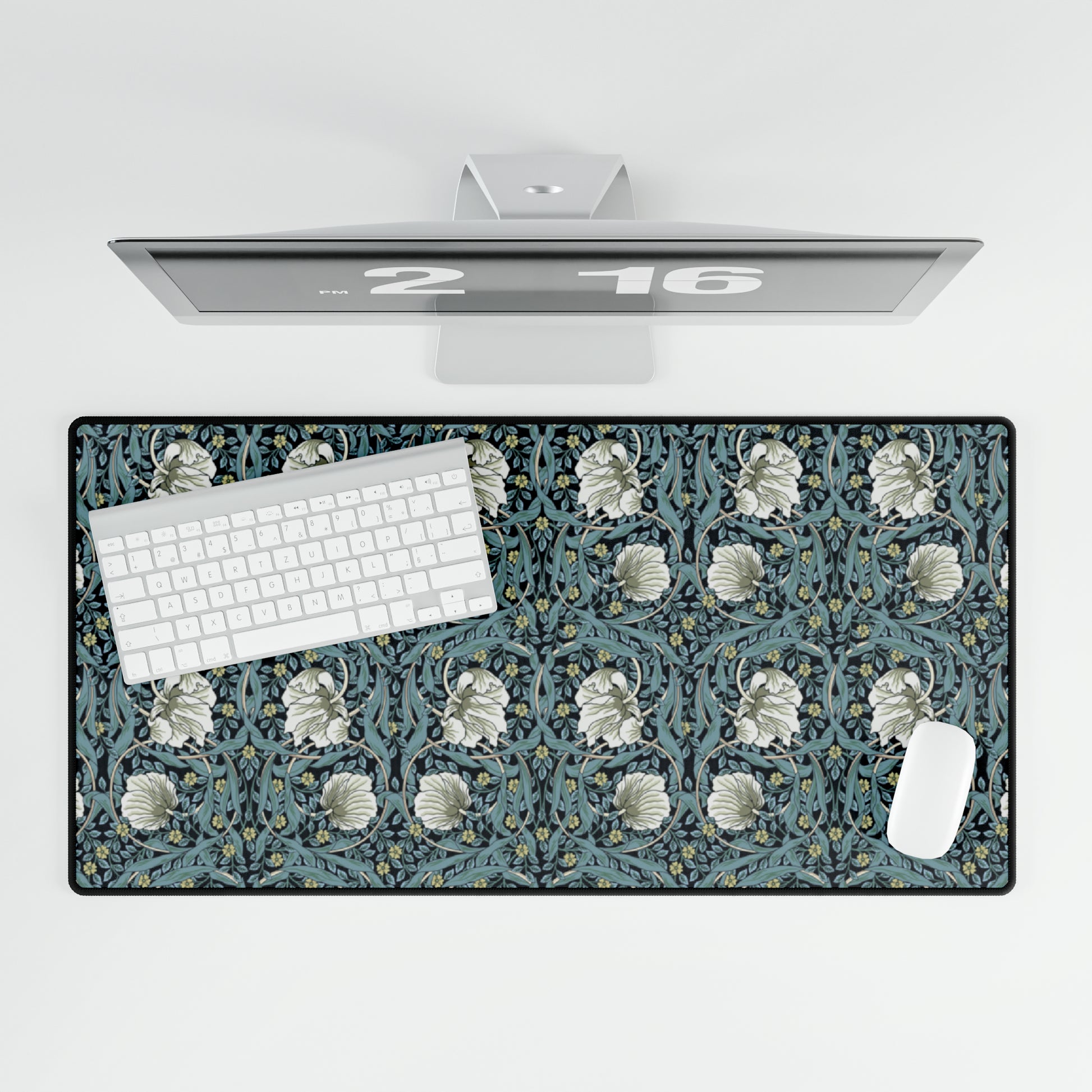 A large desk mat with a William Morris & Co floral pattern in shades of gray and blue, displayed on a desk with a keyboard and mouse.