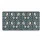 A large desk mat with a William Morris & Co floral pattern in shades of gray and blue, displayed on a desk with a keyboard and mouse.