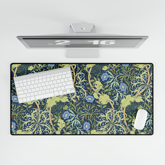 A large desk mat with a blue floral William Morris & Co pattern displayed under a monitor and accompanied by a keyboard and mouse.