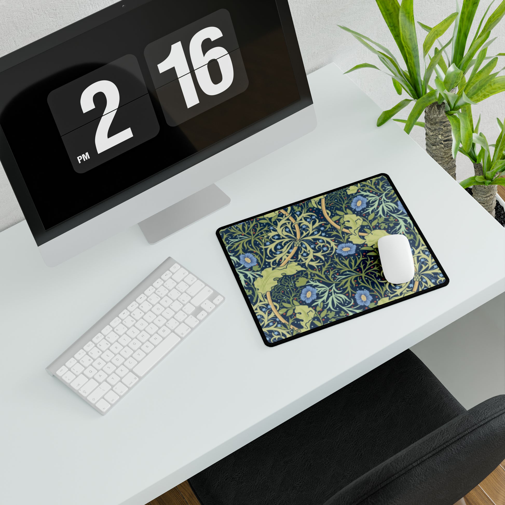 A large desk mat with a blue floral William Morris & Co pattern displayed under a monitor and accompanied by a keyboard and mouse.