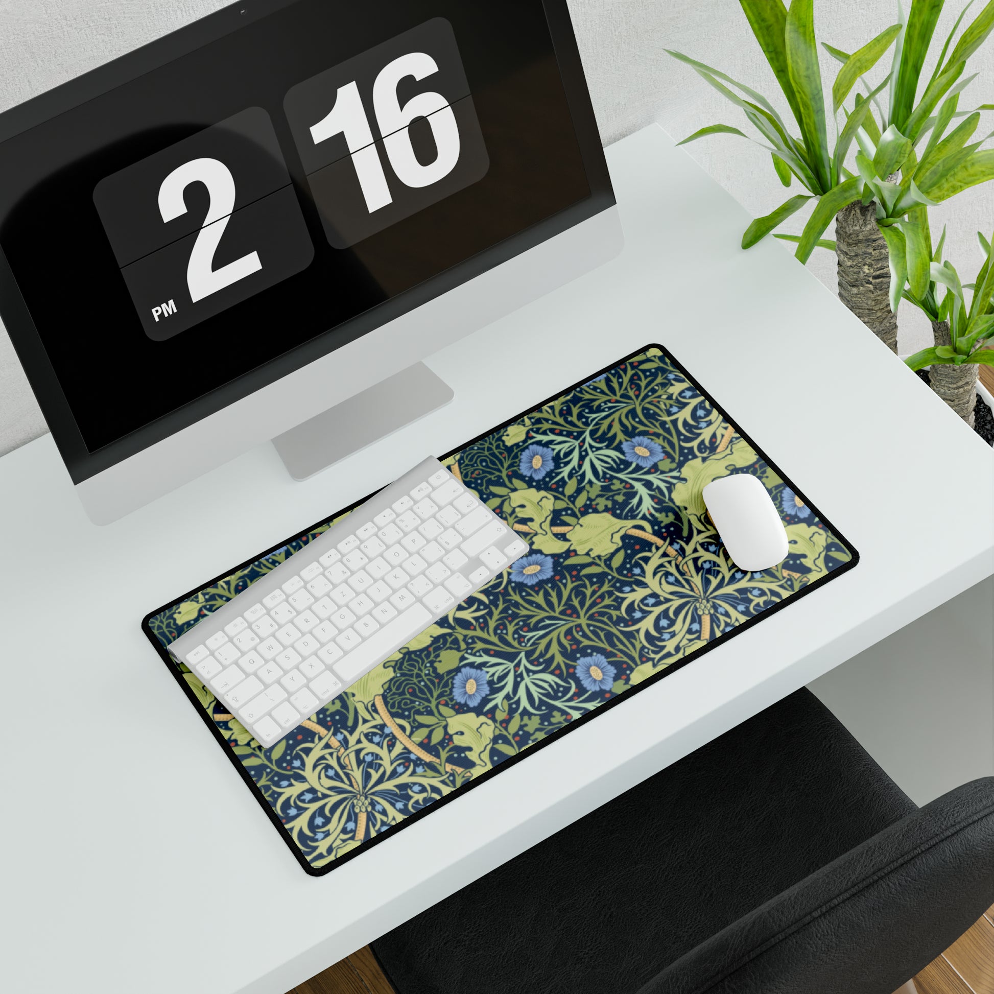 A large desk mat with a blue floral William Morris & Co pattern displayed under a monitor and accompanied by a keyboard and mouse.