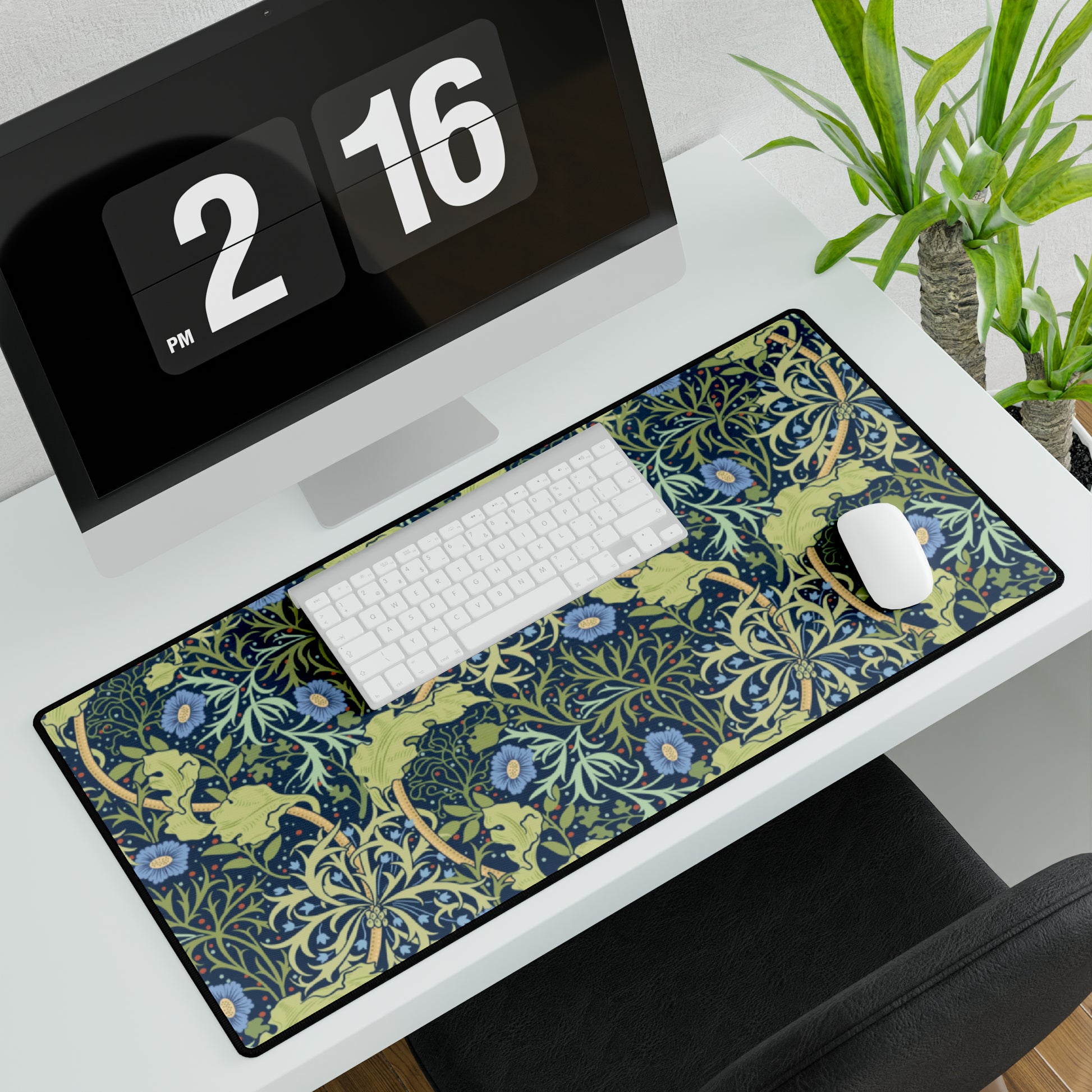 A large desk mat with a blue floral William Morris & Co pattern displayed under a monitor and accompanied by a keyboard and mouse.