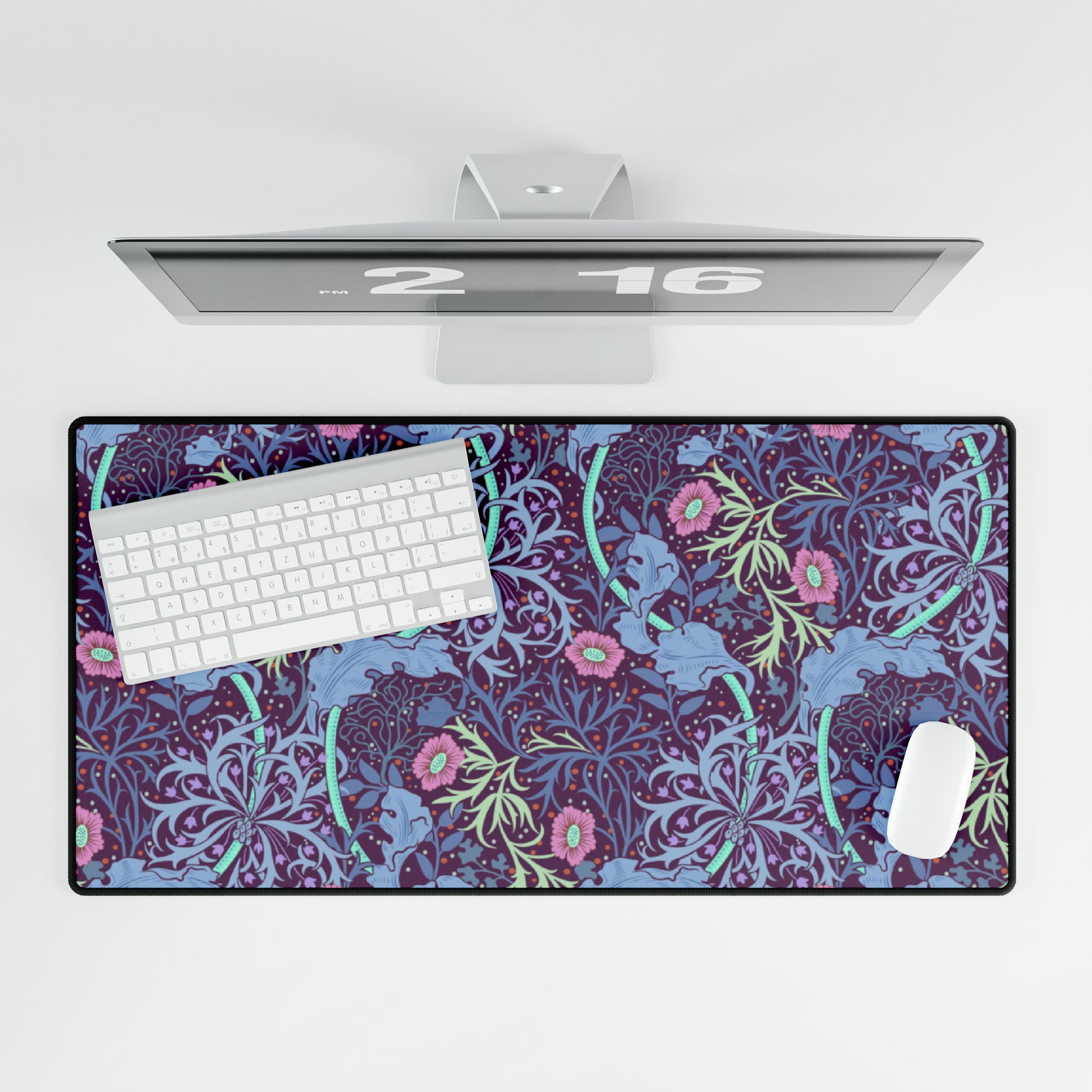 A large desk mat with a floral William Morris & Co pattern, displayed on a desk with a keyboard and mouse, with a monitor above it.