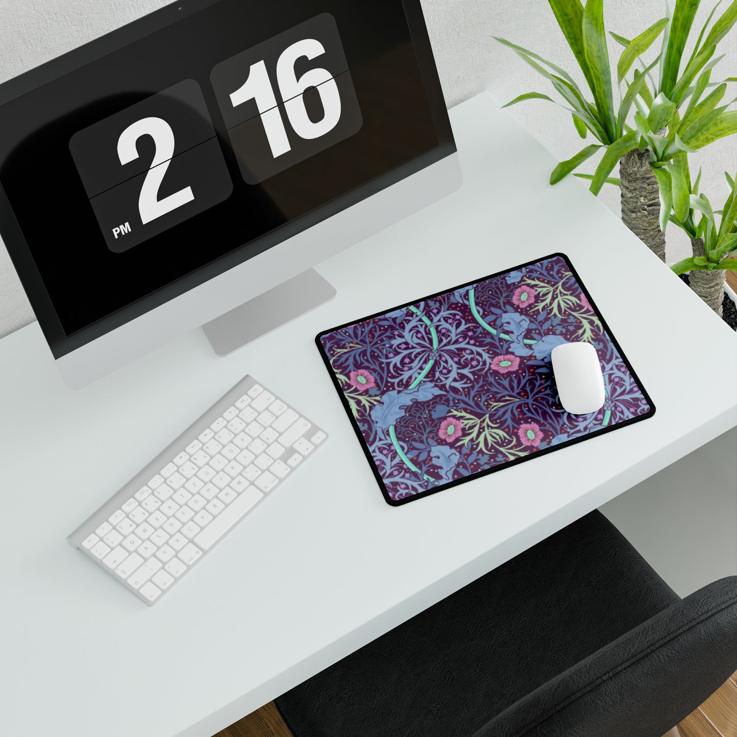 A large desk mat with a floral William Morris & Co pattern, displayed on a desk with a keyboard and mouse, with a monitor above it.