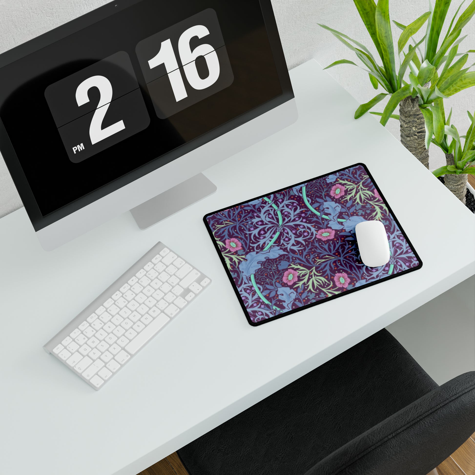 A large desk mat with a floral William Morris & Co pattern, displayed on a desk with a keyboard and mouse, with a monitor above it.
