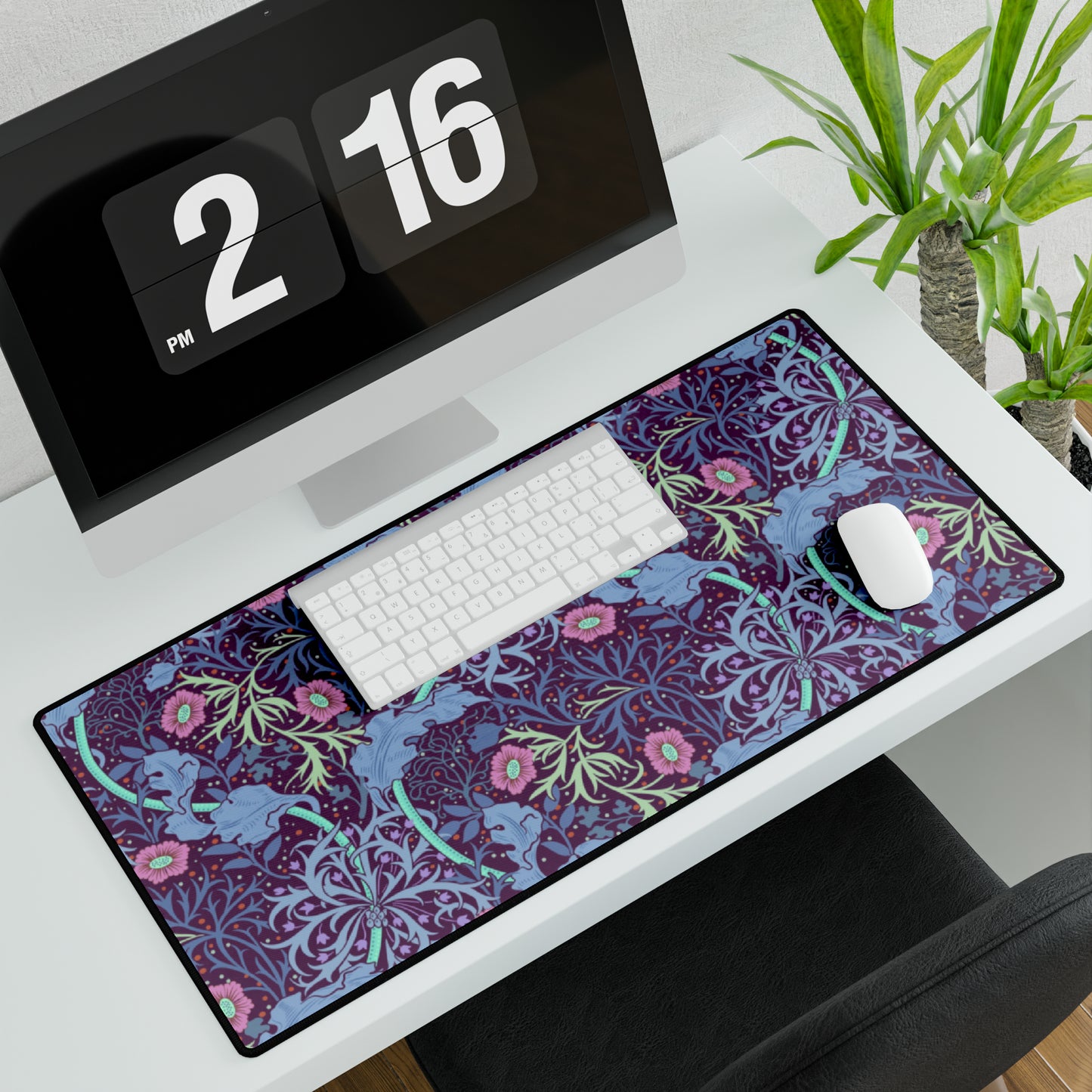 A large desk mat with a floral William Morris & Co pattern, displayed on a desk with a keyboard and mouse, with a monitor above it.