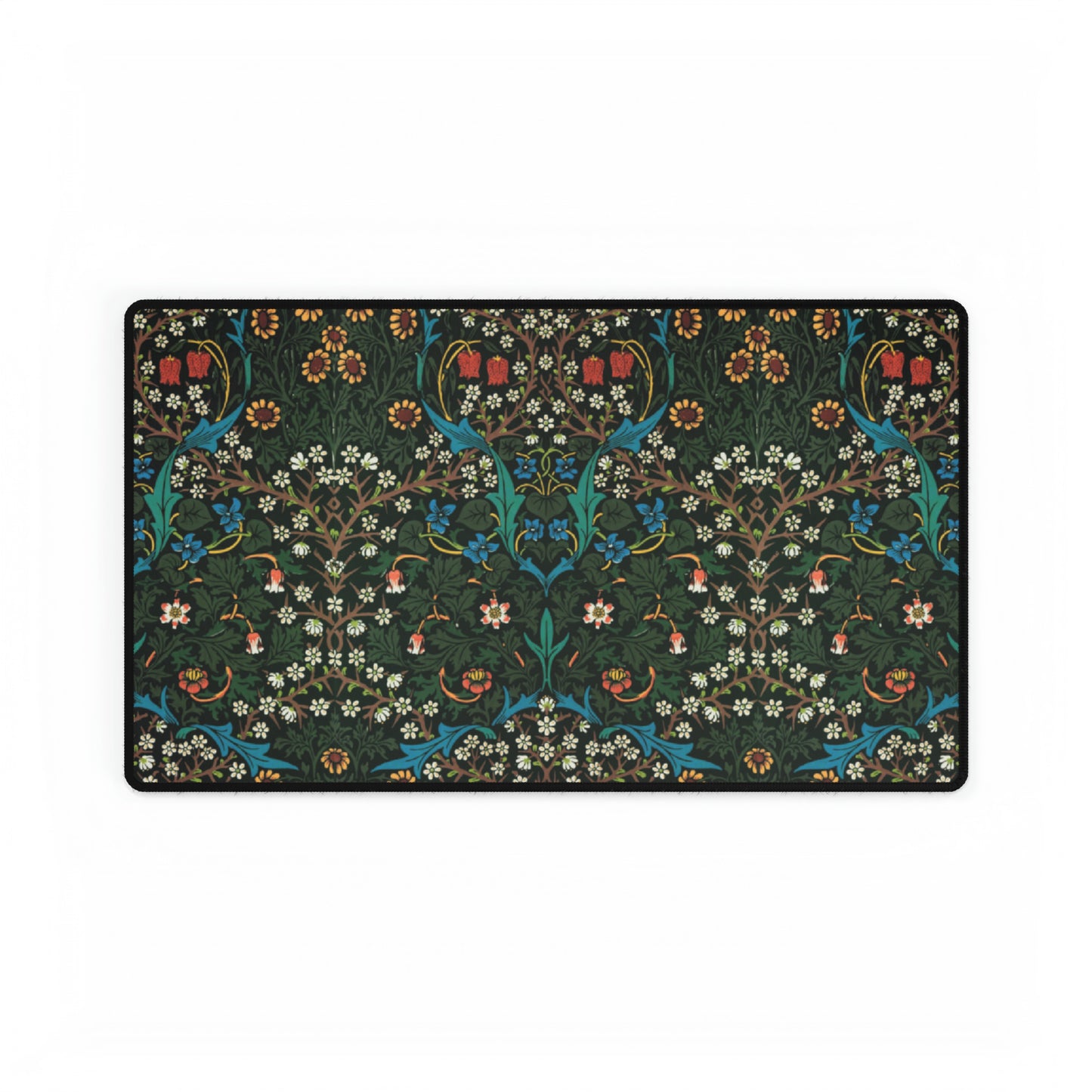 A rectangular desk mat with a William Morris & Co floral tulip pattern in red, black, and green, placed under a white desk lamp and a white keyboard.
