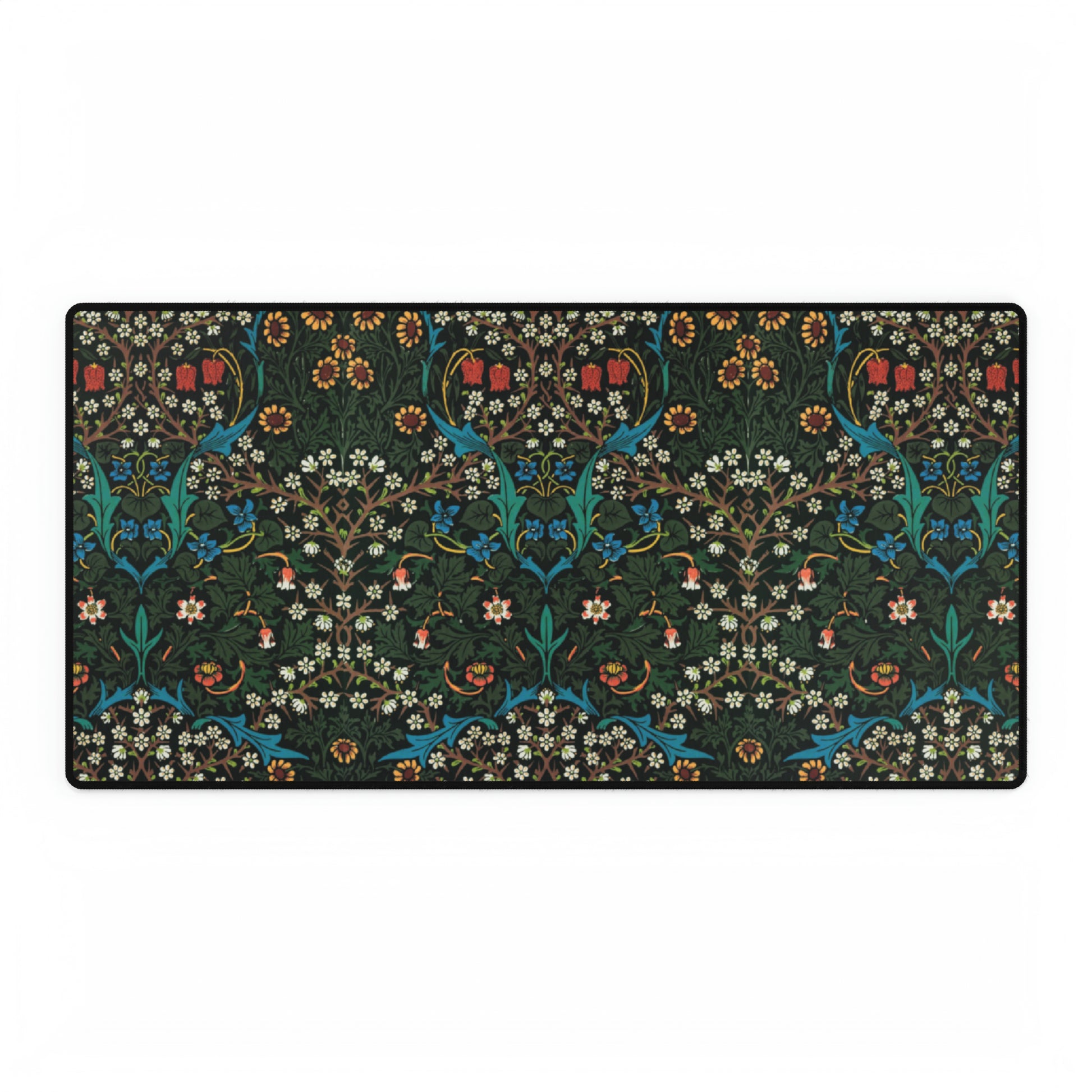 A rectangular desk mat with a William Morris & Co floral tulip pattern in red, black, and green, placed under a white desk lamp and a white keyboard.