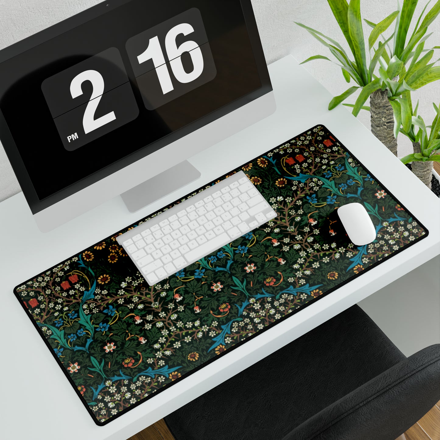 A rectangular desk mat with a William Morris & Co floral tulip pattern in red, black, and green, placed under a white desk lamp and a white keyboard.