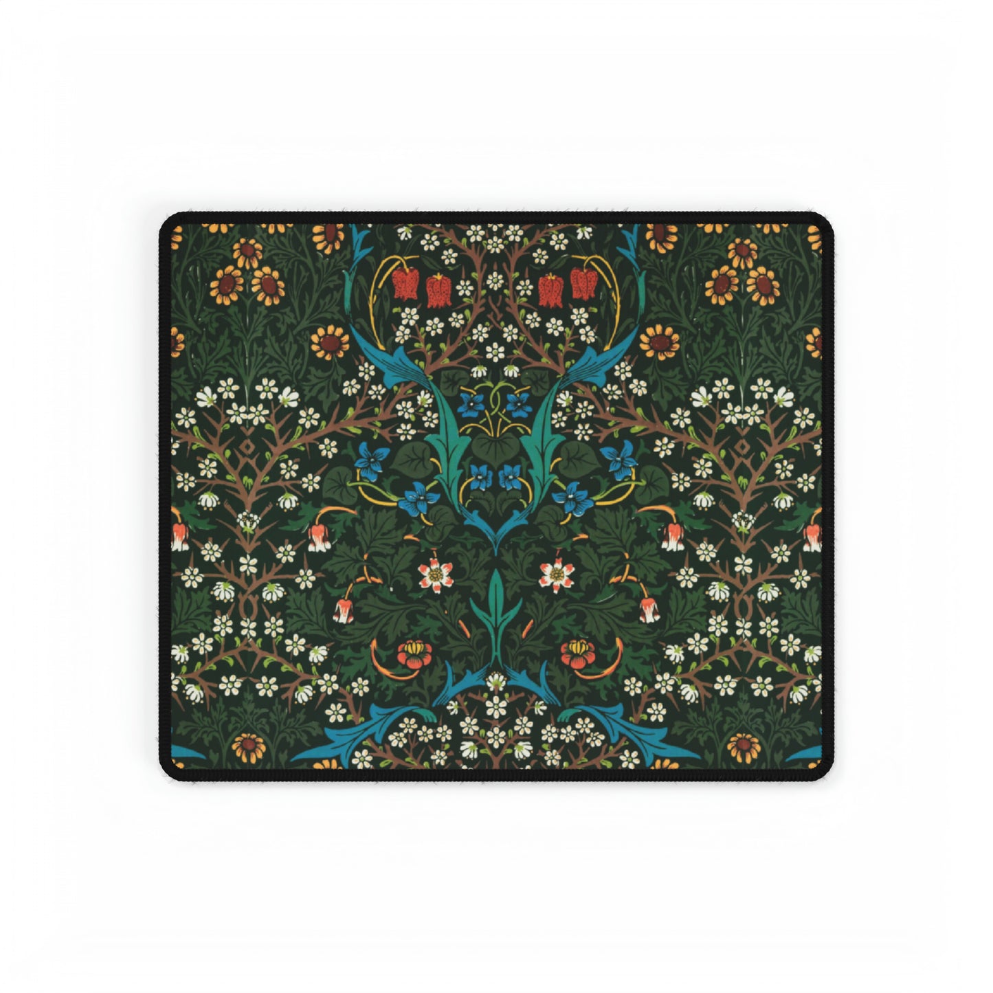 A rectangular desk mat with a William Morris & Co floral tulip pattern in red, black, and green, placed under a white desk lamp and a white keyboard.