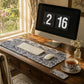 Wooden desk with computer, keyboard, mouse, and tea set near a window.