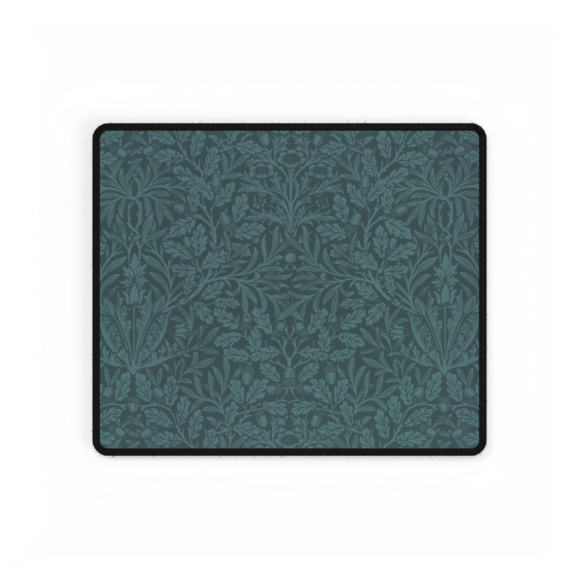 A rectangular desk mat with a teal background and an intricate floral pattern of acorns and oak leaves.