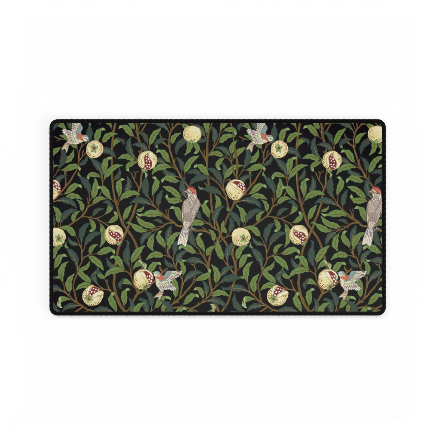 A rectangular desk mat with a floral William Morris & Co pattern featuring birds and pomegranates, placed under a desk with a keyboard and mouse on top.